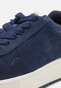 Baskets en daim bleu marine avec surface texturée, lacets ronds et semelle en caoutchouc blanche. Présente un subtil logo sur le côté et des accents cousus.