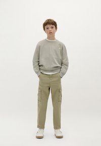 Grijze sweatshirt met een geribbelde onderrand, voorzien van een klein geel logo, gecombineerd met beige cargobroeken en witte sneakers. Eenvoudige, relaxte pasvorm.