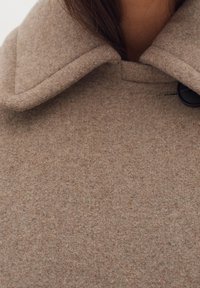 Brown wool blend coat with a large collar, textured fabric, and a button closure at the neck. Soft, warm material in a neutral tone.