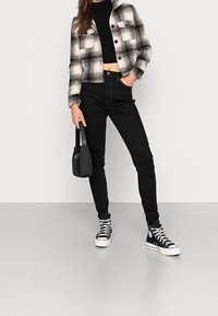 Chaqueta corta de cuadros en blanco y negro, jeans ajustados negros, zapatillas de caña alta negras con suelas blancas y un pequeño bolso negro.