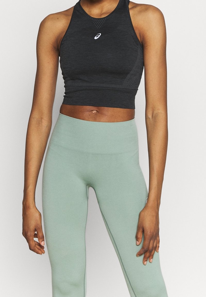 Černý sportovní crop top s fitted designem a texturovaným povrchem. V kombinaci s vysokými světle zelenými legínami s hladkým materiálem.