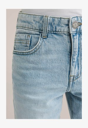 Jeans in denim azzurro chiaro con un aspetto slavato, dotati di una tasca posteriore singola, cuciture arancioni e chiusura con bottone in metallo.