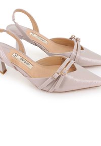 Tacones slingback sintéticos de punta afilada, en color rosa claro, con un bajo tacón bloque, correas decorativas y hebillas en tono dorado en la parte superior.
