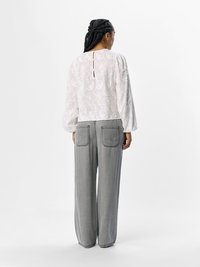 Blusa bianca ricamata con maniche a sbuffo e apertura a chiave sul retro, abbinata a pantaloni in denim grigi larghi con due tasche posteriori.