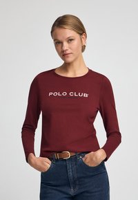 Långärmad burgundy skjorta med "POLO CLUB"-logotyp i vitt, tillverkad av mjukt tyg, med rund hals och avslappnad passform.