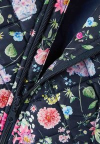 Gevoerde vest met een bloemenpatroon op een donkere achtergrond, met een zwarte rits en contrasterende stiksels.