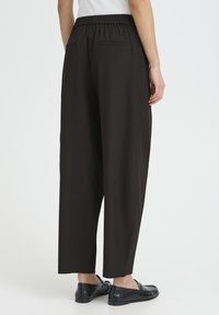 Pantalones negros con cintura elástica y corte relajado, con dos bolsillos traseros y textura suave; combinados con mocasines negros.