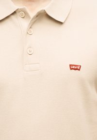 Polo beige à col avec trois boutons et un petit logo rouge Levi's sur la poitrine gauche.