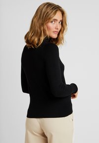 Pull noir à manches longues, moulant et doté d'un col haut, de poignets côtelés et d'un ourlet. Le matériau semble doux avec une texture lisse.