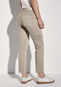 Světle béžové kalhoty slim fit, s zadními kapsami a boční kapsou na cargo, spárované s bílými teniskami a jednoduchou košilí.