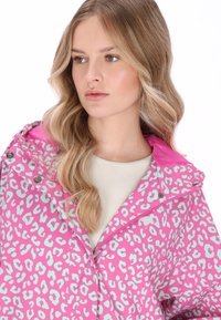 Világos rózsaszín esőkabát világoskék leopárdmintával, cipzáras elöl, és texturált belső kapucnival. Sima anyag, patentokkal záródik.