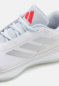 Chaussure de sport bleu clair avec un dessus en maille respirante, des accents gris, trois bandes réfléchissantes et une marque rouge sur le col.