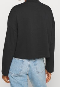 Svart kort sweatshirt med långa ärmar, tillverkad av mjukt tyg. Slät textur med avslappnad passform, kombinerad med ljusblå jeans.