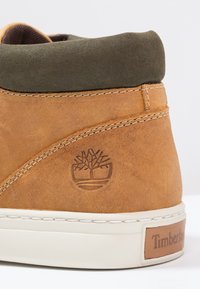 Bruna läderhöga sneakers med en krage i grön mocka, vit mellansula och präglad logotyp. Detaljerad sömnad längs sömmarna.