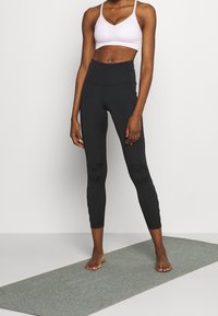 Leggings neri a vita alta e reggiseno sportivo rosa chiaro. I leggings sono aderenti e lisci; il reggiseno ha spalline sottili e una texture sottile.