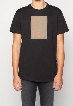 T-shirt en coton noir à manches courtes, avec un motif graphique rectangulaire beige et un texte orange, incluant des lettres stylisées "D" et "w".