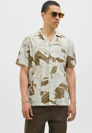 Chemise à manches courtes à boutons avec un fond clair, présentant des motifs floraux bruns, fabriquée à partir d'un tissu texturé. Portée avec un pantalon marron.