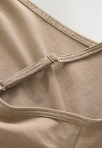 Beige bomuldsbluse med glat tekstur, justerbare stropper og et smalt bånd med kontrastsyninger langs kanterne.
