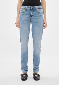 Ανάλαφρα μπλε τζιν παντελόνια με κλασική ίσια γραμμή, πέντε τσέπες και διακριτικά σημαδια φθοράς. Συνδυασμένα με μαύρα επίπεδα παπούτσια.