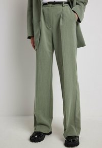 Ljusgröna vida byxor i en texturerad tyg, med veck och hög midja, kombinerade med glänsande svarta skor.