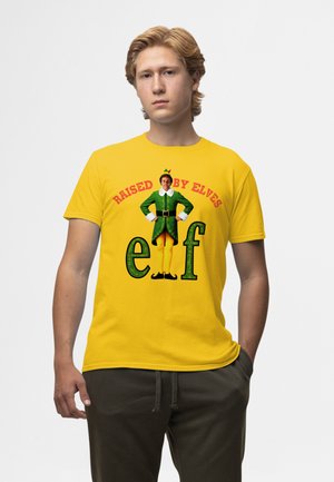Gul bomulds t-shirt med et grønt alfe grafik, rødt tekst "Raised by Elves," og "ef" i grønt. Blød struktur, afslappet pasform.