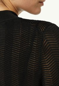 Schwarzes Strickkleid mit Chevron-Muster und offener Webstruktur. Die Textur wirkt leicht und atmungsaktiv, was das visuelle Interesse erhöht.