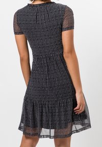 Schwarzes Kleid mit weißen vertikalen Streifen, kurzen Netzärmeln, tailliertem Oberteil und gerafftem Saum. Der strukturierte Stoff verleiht dem Design Tiefe.