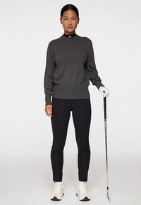 Grå stickad tröja med rund hals, ribbade muddar och fåll, ihop med tajta svarta byxor. Figuren håller i en golfklubba och bär vita skor.