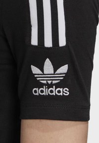 Svart tygärmar med tre vita vertikala ränder och vitt broderat Adidas Trefoil-logotyp ovanför varumärkesnamnet.