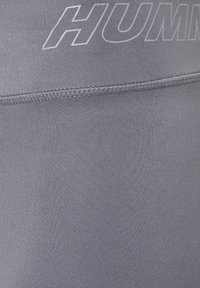 Leggings de sport gris avec une texture de tissu lisse, dotés d'une large ceinture et d'un logo réfléchissant imprimé sur le devant.