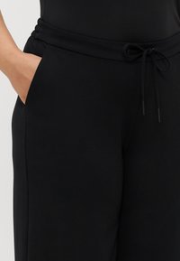 Pantalons de survêtement noirs avec une texture douce, une taille élastique et un cordon de serrage. Comprend des poches latérales. Design simple sans motifs ni embellissements.