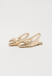 Chaussures slingback dorées à bout pointu, avec des détails entrecroisés et un petit nœud sur le devant. Semelle plate.
