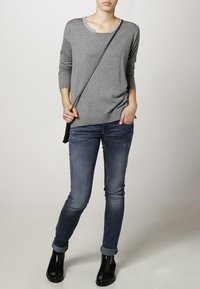 Grauer Strickpullover mit Rundhalsausschnitt und strukturiertem Saum. Kombiniert mit enganliegenden dunkelblauen Jeans und schwarzen Stiefeletten.