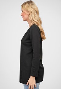 Zwart langemouwen top met een gestructureerd ribbelontwerp, met een relaxte pasvorm en een afgeronde zoom, gestyled over lichtblauwe jeans.