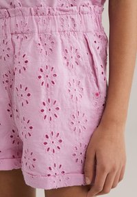 Rozā šorti, izgatavoti no auduma ar ziedu izgriezumu rakstiem, ar elastīgu jostasvietu un sānu kabatām. Gluda virsma ar detalizētu izšuvumu.