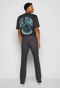 Czarny t-shirt z dużą turkusową grafiką "LEE JEANS" na plecach, w zestawie z ciemnoszarymi prostymi dżinsami i czarnymi trampkami.