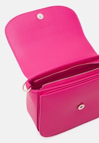 Růžová texturovaná kožená kabelka s magnetickým uzávěrem a kapsami na zip uvnitř. Vyznačuje se čistými liniemi a strukturovaným tvarem.