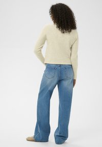 Beiger Strickpullover mit langen Ärmeln, kombiniert mit hellblauen weiten Jeans, zeigt die Rückansicht und ein glattes, lässiges Design.