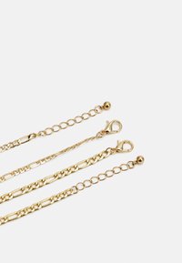 Correntes de metal dourado de comprimentos variados, com elos lisos e texturizados, dotadas de fechos de lagosta e acentos esféricos nas extremidades.