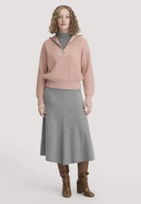 Rosa gerippter Pullover mit einem Reißverschlusskragen, kombiniert mit einem grauen knielangen Rock. Braune kniehohe Stiefel runden das Outfit ab.