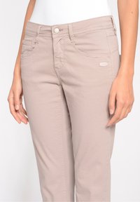 Ljust beige byxor gjorda av bomullsblandat tyg. Har fem fickor, knappstängning och subtila sömnadsdetaljer längs sömmarna.