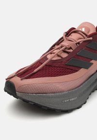 Scarpa da corsa rossa e rosa con tomaia in rete, strisce nere, dettagli testurizzati e una spessa suola in gomma grigia etichettata 'LIGHT BOOST'.