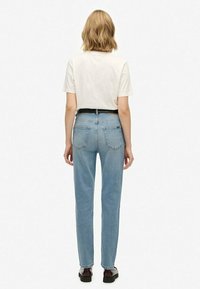 Jeans de mezclilla de color azul claro con un corte recto, que presentan una cintura de media altura, bolsillos traseros y un cinturón negro, combinados con una camiseta blanca.