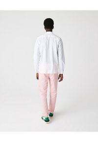Camisa blanca de manga larga, pantalones rosas y zapatillas verdes, vista desde atrás. La camisa tiene cuello; los pantalones son ajustados.