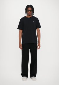 Tricou din bumbac negru cu mâneci scurte, combinat cu pantaloni largi negri. Adidași albi și ochelari de soare închiși la culoare completează ținuta.