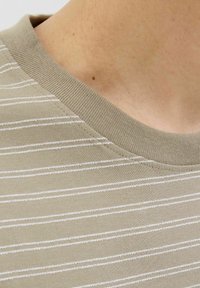 Beige fabric t-shirt featuring white horizontal stripes, a round crew neckline, and textured knit details along the collar and hem.