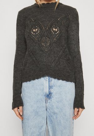 Jersey de punto gris oscuro con patrones calados en forma de diamante combinado con vaqueros de talle alto azul claro en una persona.