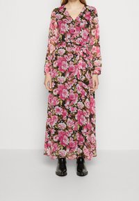 Blommig maxiklänning med långa ärmar och V-ringning, prydd med rosa och vita blommor mot en svart bakgrund, knuten i midjan.