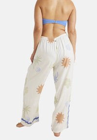White, lightweight cotton pants with a loose fit. Features tropical patterns in soft colors—peach, green, and blue—with an elastic waistband.