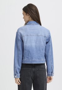 Lichtblauwe denim jas met een cropped ontwerp, voorzien van een klassieke kraag en knoopmanchetten, gecombineerd met zwarte jeans.